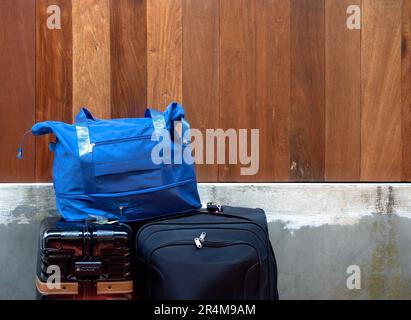 Bagaglio blu impilato su grandi bagagli neri e zaino su pareti di legno e cemento con spazio per le copie. Foto Stock