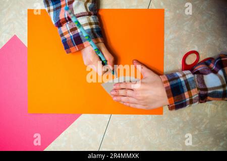 Vista ravvicinata delle mani di un bambino che tracciano la foglia su carta di colore brillante Foto Stock