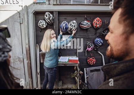 Una giovane donna afferra due caschi da bici appesi a una parete Foto Stock