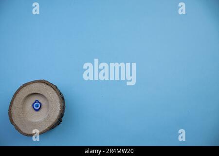 Piccolo tronco fotografato dall'alto, collocato sul bordo dello sfondo blu, con il cordone di occhio malvagio all'interno Foto Stock