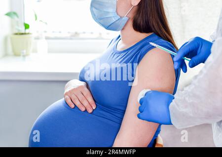 Vaccinazione in gravidanza. Donna incinta in maschera facciale vaccinata in clinica. Medico che dà vaccino Corona Virus iniezione paziente in Clinic. Popula Foto Stock