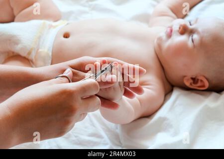 Il bambino che ottiene le unghie tagliate mentre dorme dalla sua madre con le forbici. Allattare un bambino. Ritaglio. Come agganciare con successo le unghie del bambino neonato. Foto Stock