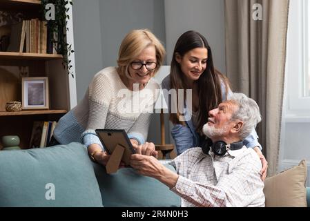 Felice famiglia di tre-generazione che abbraccia sedersi al coperto godere del tempo insieme a casa, ridendo figlia cresciuta con 70s papà e 50s mamma di mezza età caldo re Foto Stock
