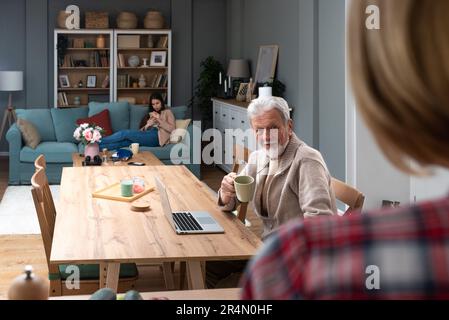 Felice famiglia di tre-generazione che abbraccia sedersi al coperto godere del tempo insieme a casa, ridendo figlia cresciuta con 70s papà e 50s mamma di mezza età caldo re Foto Stock