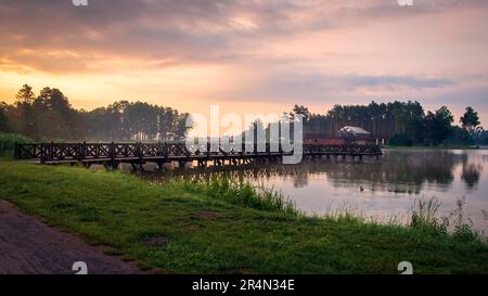 Un bel ponte in legno sul lago di Krasnobród. Alba sul lago. Pineta sullo sfondo. Krasnobrod, Roztocze, Polonia Foto Stock