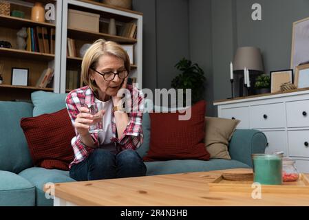 Penosa pensosa donna di mezza età guardando lontano sedersi da sola a casa sentirsi ansioso solo, triste depresso melancholic vecchia donna matura soffrono di dolore Foto Stock