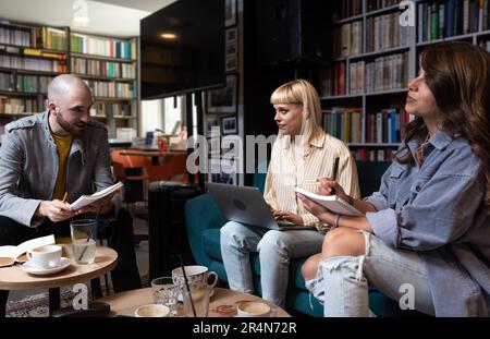 Gruppo di tre studenti universitari di generazione Z che lavorano insieme al computer portatile, scrivendo appunti, guardando il webinar di apprendimento, la lezione online, leggendo tutorial su in Foto Stock