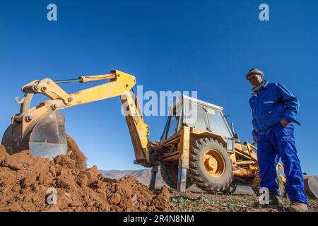 Coltivatore che utilizza un retroescavatore per preparare il suo campo per la piantagione di Almond Tree Foto Stock