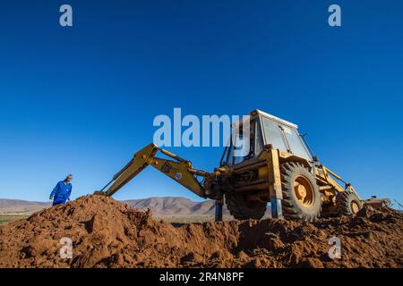 Preparazione del terreno: Farmer gestisce un Digger per creare buchi di semina per gli alberi di mandorle Foto Stock