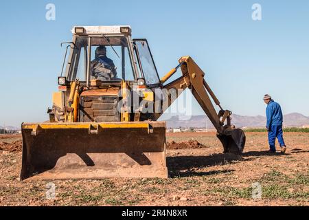 Contadino che manipola una pala caricatrice per stabilire i punti di semina per gli alberi di mandorle nel suo campo Foto Stock