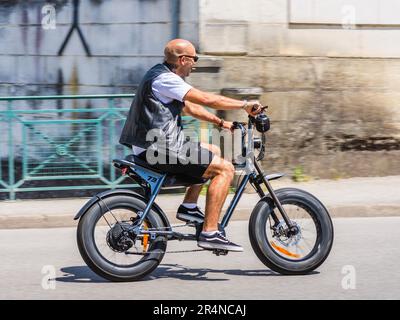 Calvo uomo, fumo ciger, velocità lungo la strada su Super-73 bici elettrica - Loches, Indre-et-Loire (37), Francia. Foto Stock