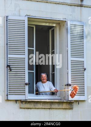 Donna matura che scuote spazzolone polveroso fuori dalla finestra aperta - Loches, Indre-et-Loire (37), Francia. Foto Stock