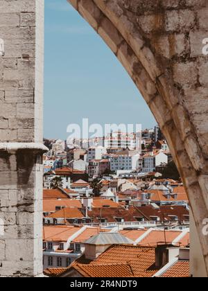 Vista degli edifici della città con tetti in tegole a Lisbona attraverso un arco in un antico muro di pietra, Lisbona, Portogallo Foto Stock