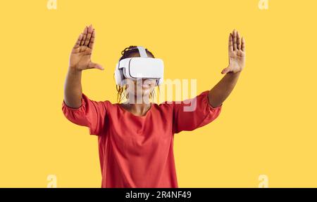 Giovane donna in occhiali VR esplora il cyberspazio giocando a realtà virtuale su sfondo giallo. Foto Stock