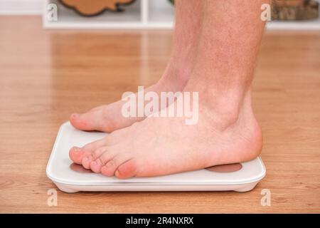 Un uomo si trova sulla bilancia. Il ragazzo sta pesando se stesso. Bilance da pavimento per la salute. Controllo del peso. Foto Stock