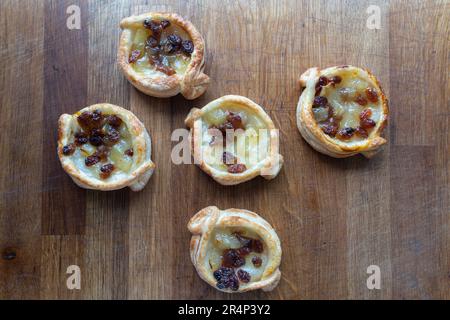 Un delizioso assortimento di dolci danesi al puff con una deliziosa combinazione di mela e uva sultanina, splendidamente sistemati su un rustico choppi di legno Foto Stock