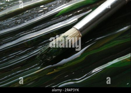 Primo piano del pennello di un artista. Pennello su uno sfondo di vernice scura bagnata. Foto Stock