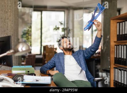 Giovane uomo felice che tiene modello di aereo in ufficio. Foto Stock