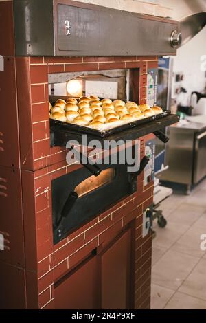 Panettiere irriconoscibile che togli dal forno il vassoio con pani gustosi. Foto Stock