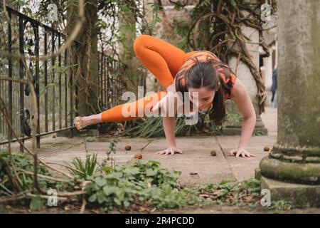 Donna caucasica nuova insegnante di yoga fare una posa libellula indossando abbigliamento sportivo arancione sulla terrazza di uno storico giardino paesaggistico a Hampstead Heath, L Foto Stock