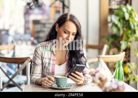 Ritratto di bella donna utilizzando il suo smartphone in caffè, legge i messaggi ricevuti e segue i social network. Foto Stock