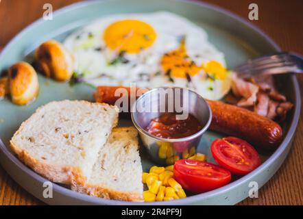 Uova fritte con salsicce, pomodoro e pane sul piatto. Colazione inglese nel caffè. Tavolo europeo per la colazione. Uova con carne e verdure. Foto Stock