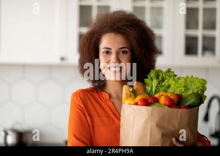 Giovane donna afroamericana sorridente che tiene la borsa di carta piena di generi alimentari Foto Stock