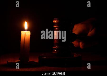 Una mano tiene un gavel di corte nel buio vicino ad una candela, la corte più alta, legge Foto Stock