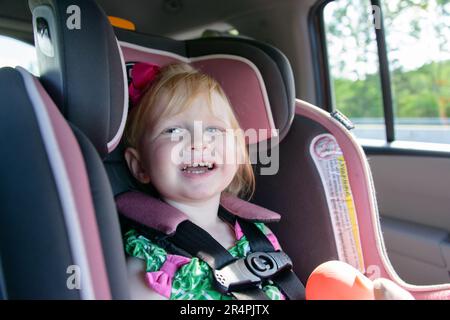 Ragazza sorridente di due anni in carseat durante un viaggio su strada. Foto Stock
