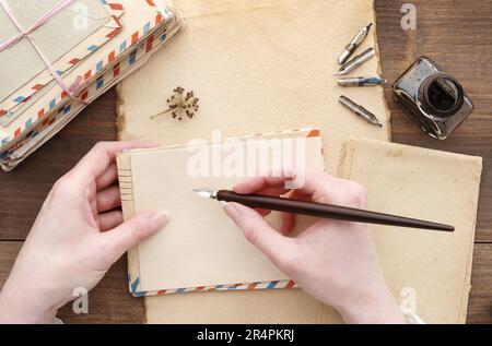 La giovane donna ha una penna vintage e un foglio di carta. Pila di vecchie lettere e inkwell in background. Foto Stock