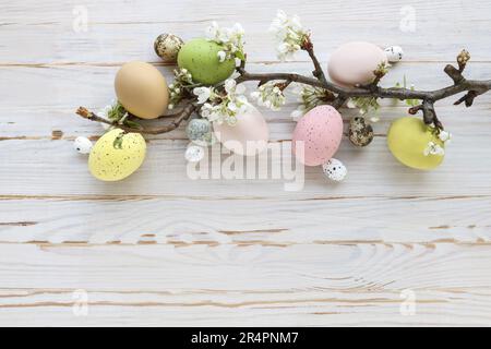 Uova di Pasqua colorate e ramo fiorito di mela su uno sfondo bianco di legno. Foto Stock