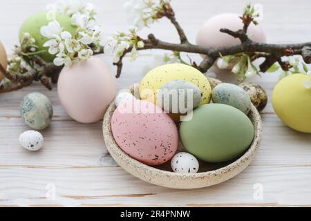 Uova di Pasqua colorate e ramo fiorito di mela su uno sfondo bianco di legno. Foto Stock