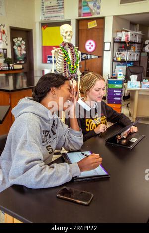 Le ragazze studentesche senior di una scuola superiore cattolica della California meridionale chiacchierano sul proprio computer portatile in una lezione di biologia. Notate lo scheletro e i logo del college Foto Stock