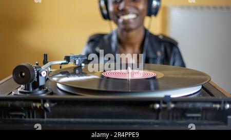 giovane donna che indossa una giacca in pelle con cuffie mentre gioca un disco in vinile su un giradischi vintage Foto Stock