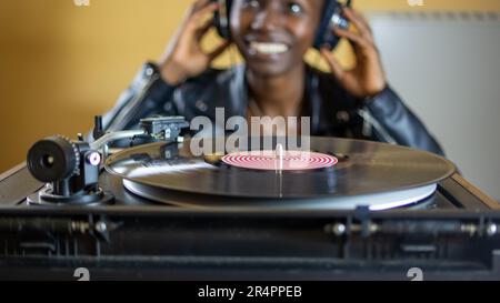 giovane donna che indossa una giacca in pelle con cuffie mentre gioca un disco in vinile su un giradischi vintage Foto Stock