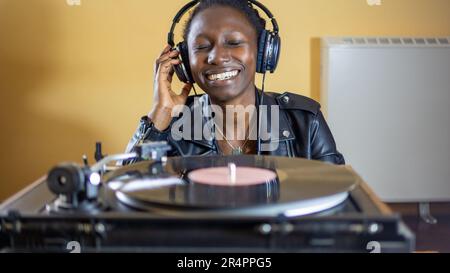 giovane donna che indossa una giacca in pelle con cuffie mentre gioca un disco in vinile su un giradischi vintage Foto Stock