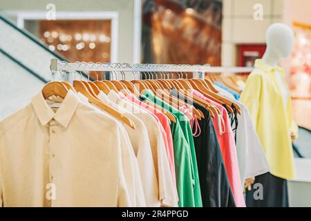Primo piano di appendiabiti con abbigliamento casual per la gioventù in negozio, tessuti naturali e colori. Sfondo sfocato astratto. Messa a fuoco selettiva Foto Stock
