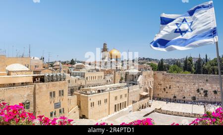 Gerusalemme, Israele; 28 maggio 2023 - una bandiera israeliana soffia al vento mentre i credenti ortodossi ebrei leggono la Torah e pregano di fronte al Muro Occidentale. Foto Stock