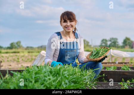 Ritratto di donna contadina sorridente con cestino di erbe rucola guardando la macchina fotografica Foto Stock