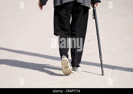 Donna anziana che cammina con la canna sulla strada della città, gambe sul marciapiede. Concetto di disabilità, adulta limping, malattie della colonna vertebrale Foto Stock