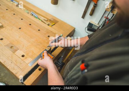 Le mani del falegname disegnano con cura la linea usando il marcatore e il righello sulla tavola di legno. Foto di alta qualità Foto Stock