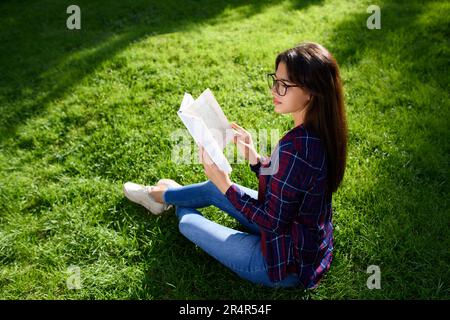 Giovane donna con libro su erba verde all'aperto Foto Stock