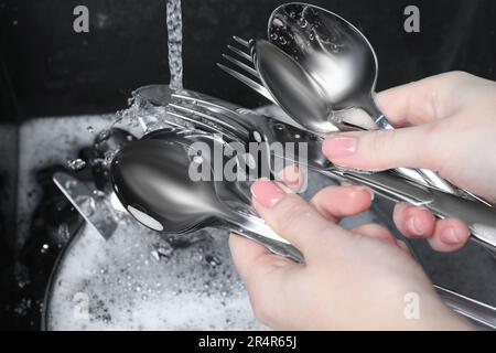 Donna che tiene utensili da cucina in argento pulito vicino al lavandino, primo piano Foto Stock