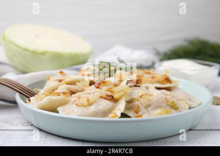 Gnocchi cotti (varenyky) con gustoso ripieno, cipolle fritte e aneto su tavola di legno, primo piano Foto Stock