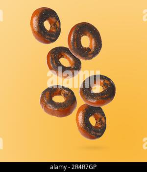 Molti bagel freschi con semi di papavero che cadono su fondo arancione chiaro Foto Stock