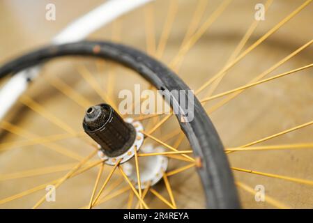 Ruota per biciclette e pneumatico senza aria smontati sul pavimento di un negozio di riparazione di biciclette. Cerchio bianco, razze arancioni, pneumatico nero. Chiudere la composizione con le copie Foto Stock