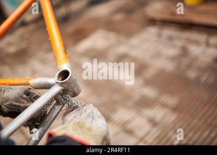 Lavoro manuale: Lavoratore irriconoscibile che utilizza lana d'acciaio su un telaio di bicicletta dopo aver passato una torcia elettrica su di esso per rimuovere la vernice, come parte della bicicletta re Foto Stock