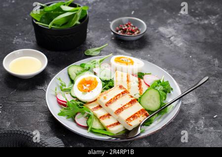 Pasto salutare al paleo Ketogenic, Halloumi alla griglia con lattuga, ravanello, cetriolo, uovo bollito su fondo scuro, Detox, pranzo dietetico Foto Stock