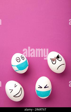 Uova bianche di Pasqua in maschera medica protettiva e due uova senza maschera su sfondo rosa. Pasqua sul concetto di quarantena con posto per il testo. Arrestare IL VIRUS Foto Stock