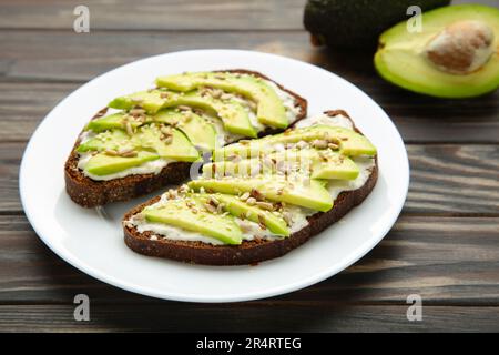 Panino di avocado su pane di segale scuro con avocado fresco a fette su fondo marrone. Vista dall'alto Foto Stock